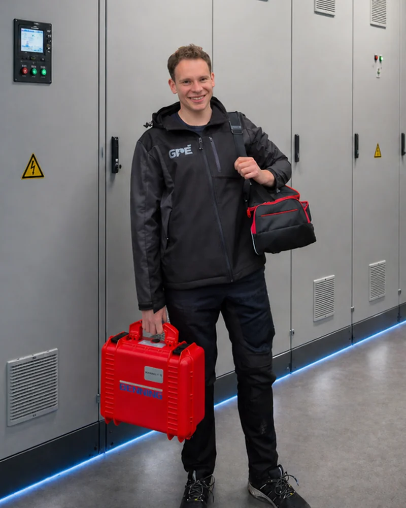 Robert Gericks vor einem Industrie-Schaltschrank mit Benning Prüfkoffer und Messtasche